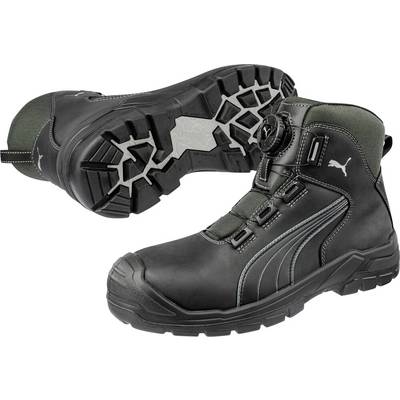 Paire de bottes de travail Puma noires et vert foncé, l'une présentée de côté et l'autre semelle vers le haut, mettant en évidence la bande de roulement robuste et le design à lacets.