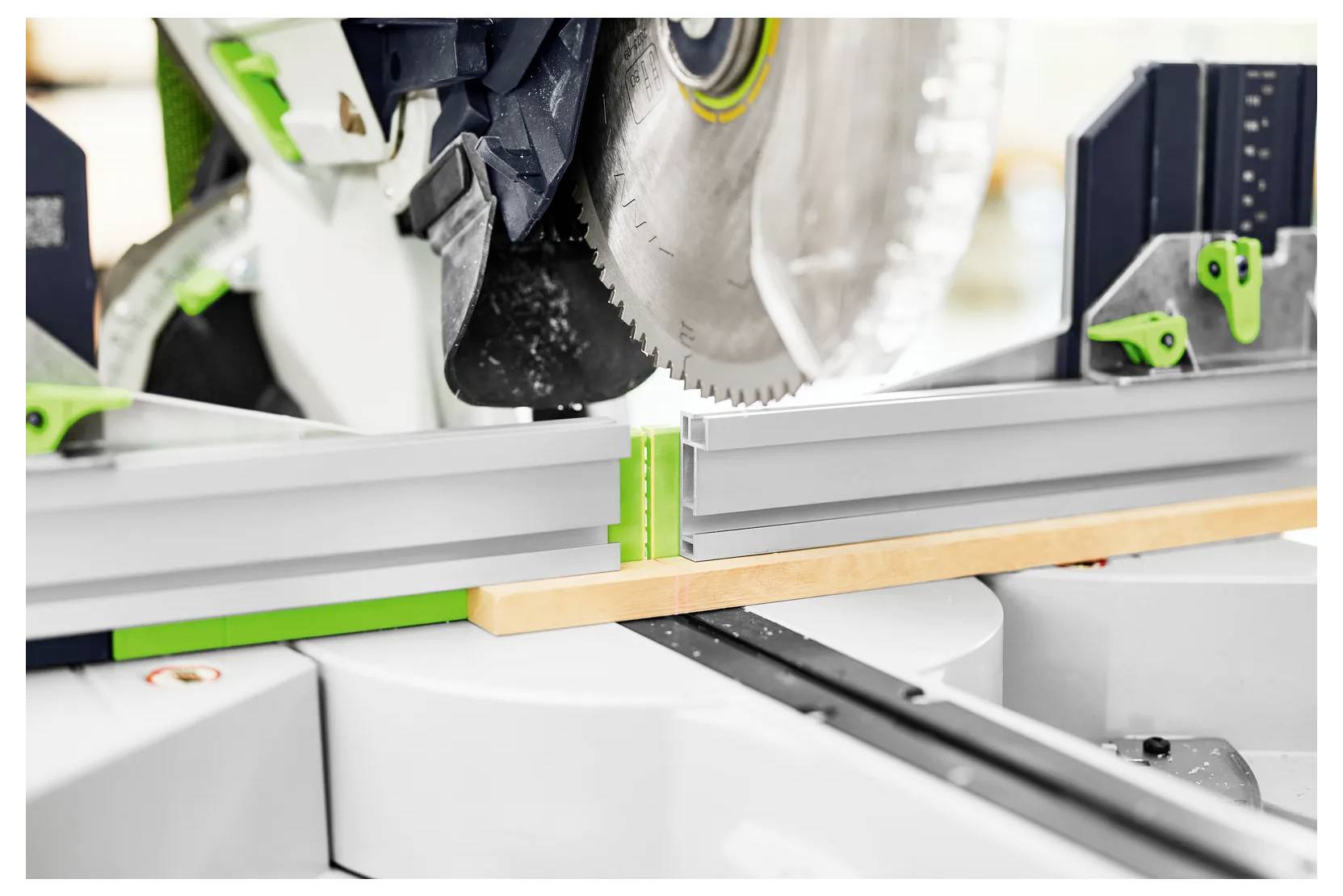 Gros plan d'une scie à onglets coupant un profil vert et blanc sur un établi dans un atelier.