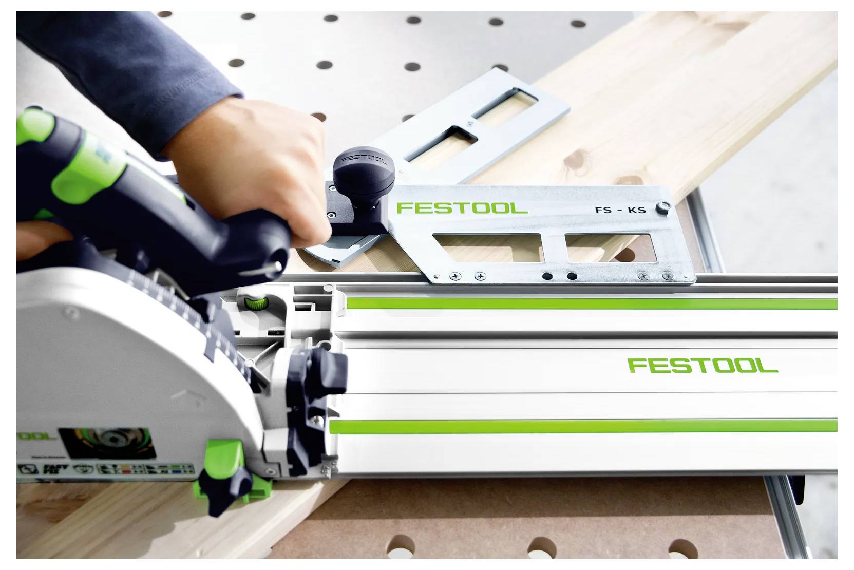 Gros plan d'une personne utilisant une scie circulaire Festool avec rail de guidage pour couper une planche de bois sur un établi.