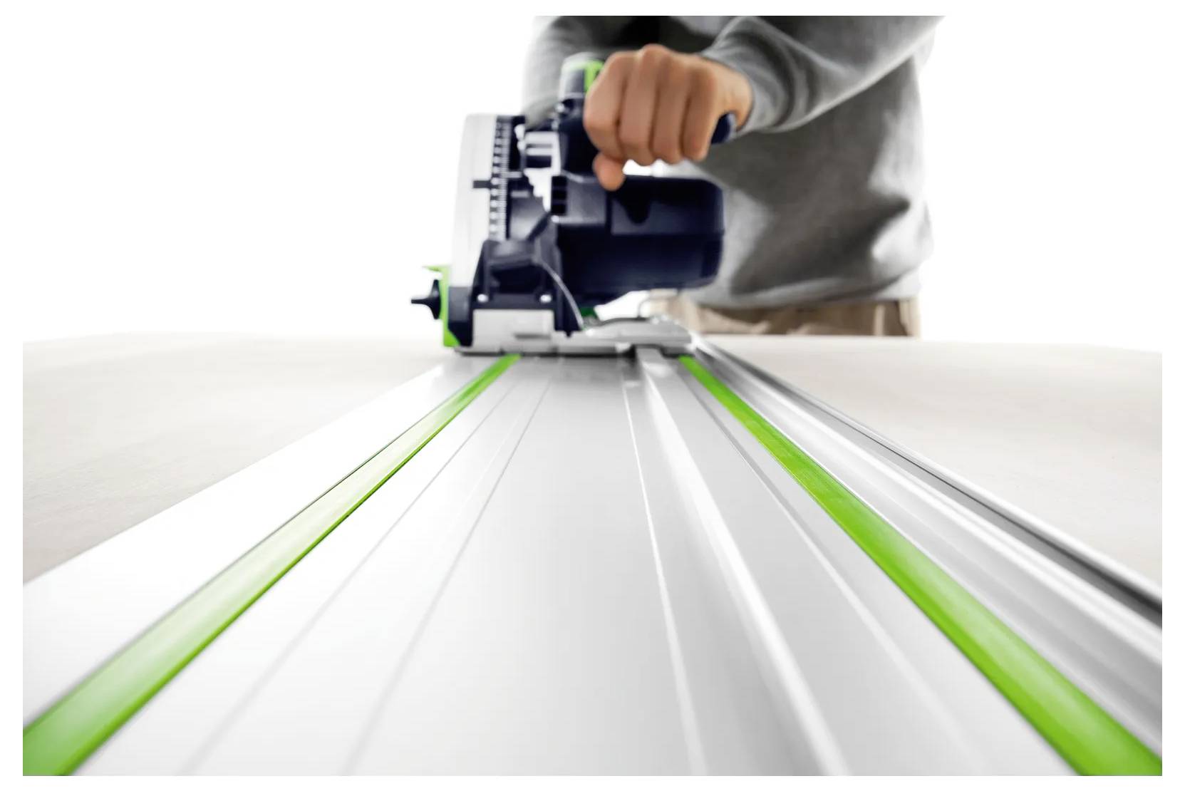 Personne utilisant une scie circulaire pour couper une longue planche ou feuille le long d'une ligne de guidage droite, avec des bandes de guidage vertes visibles.
