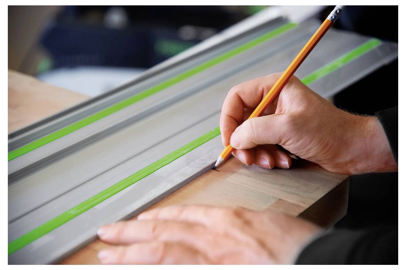 Une personne utilise un crayon et une règle pour marquer une pièce de bois, avec des bandes de guide vertes sur un établi pendant des travaux de menuiserie.