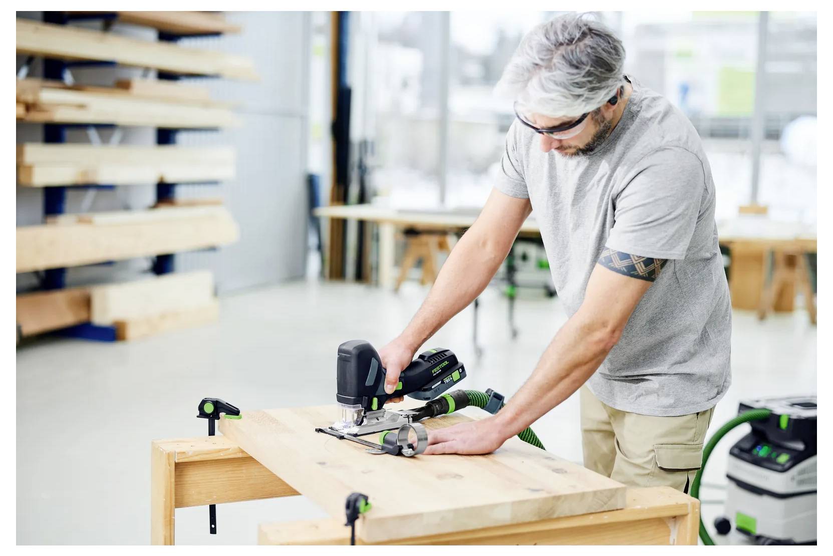 Un charpentier dans un atelier coupe une planche de bois avec une scie électrique sur un établi.