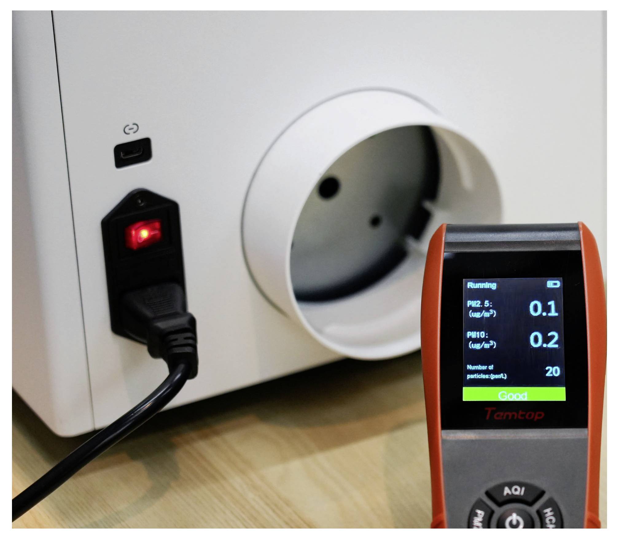 Purificateur d'air avec cordon d'alimentation branché à côté d'un capteur de qualité de l'air portatif affichant « Bon » et les lectures de particules.
