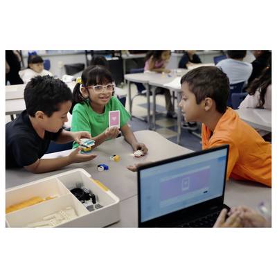 Des enfants dans une salle de classe collaborent autour de petits blocs de construction sur une table tandis qu'un ordinateur portable est ouvert au premier plan.