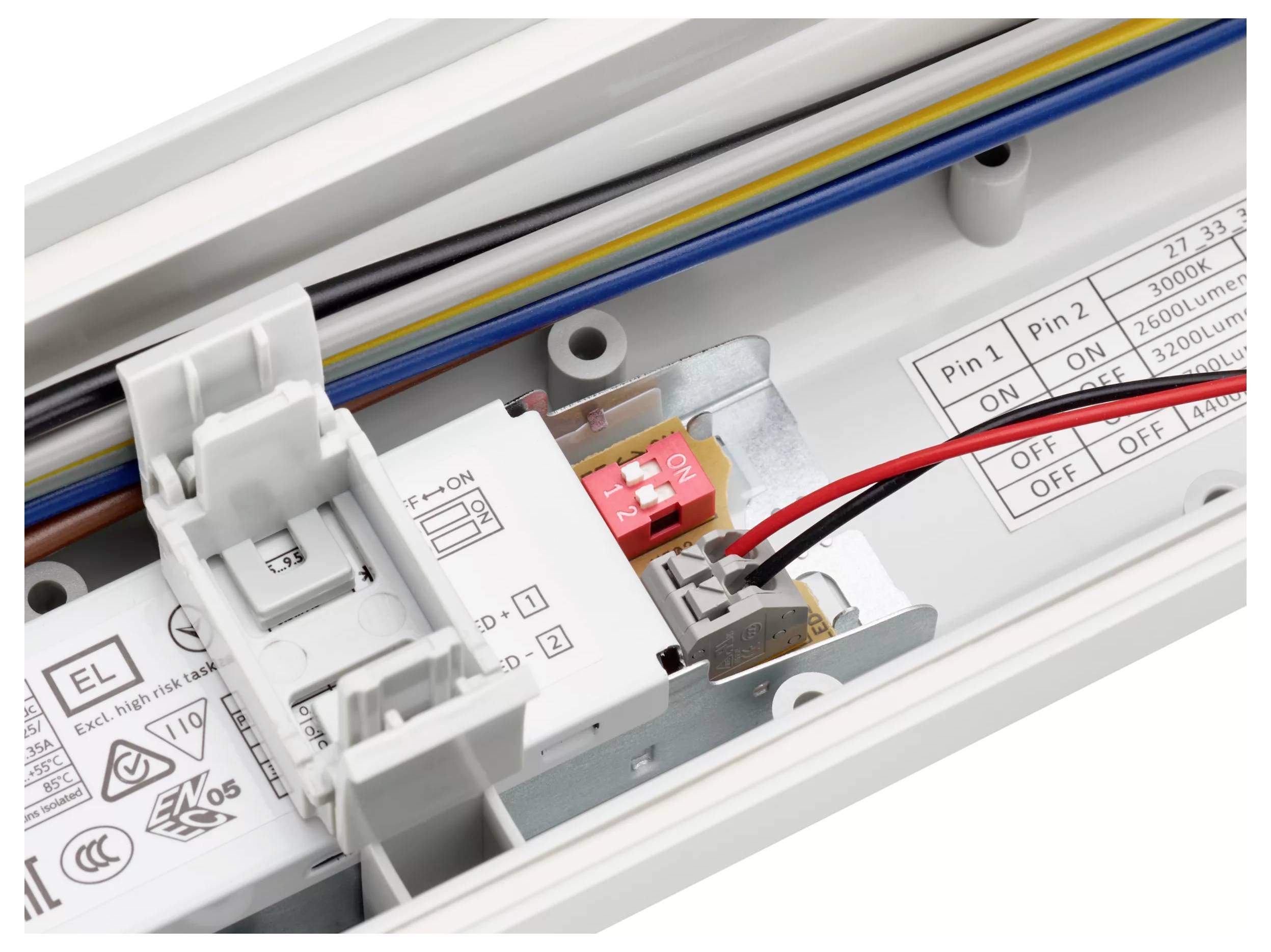 Gros plan d'un panneau de commande d'appareil électrique avec un interrupteur marche/arrêt rouge, des fils connectés et des circuits imprimés et des étiquettes de réglage.