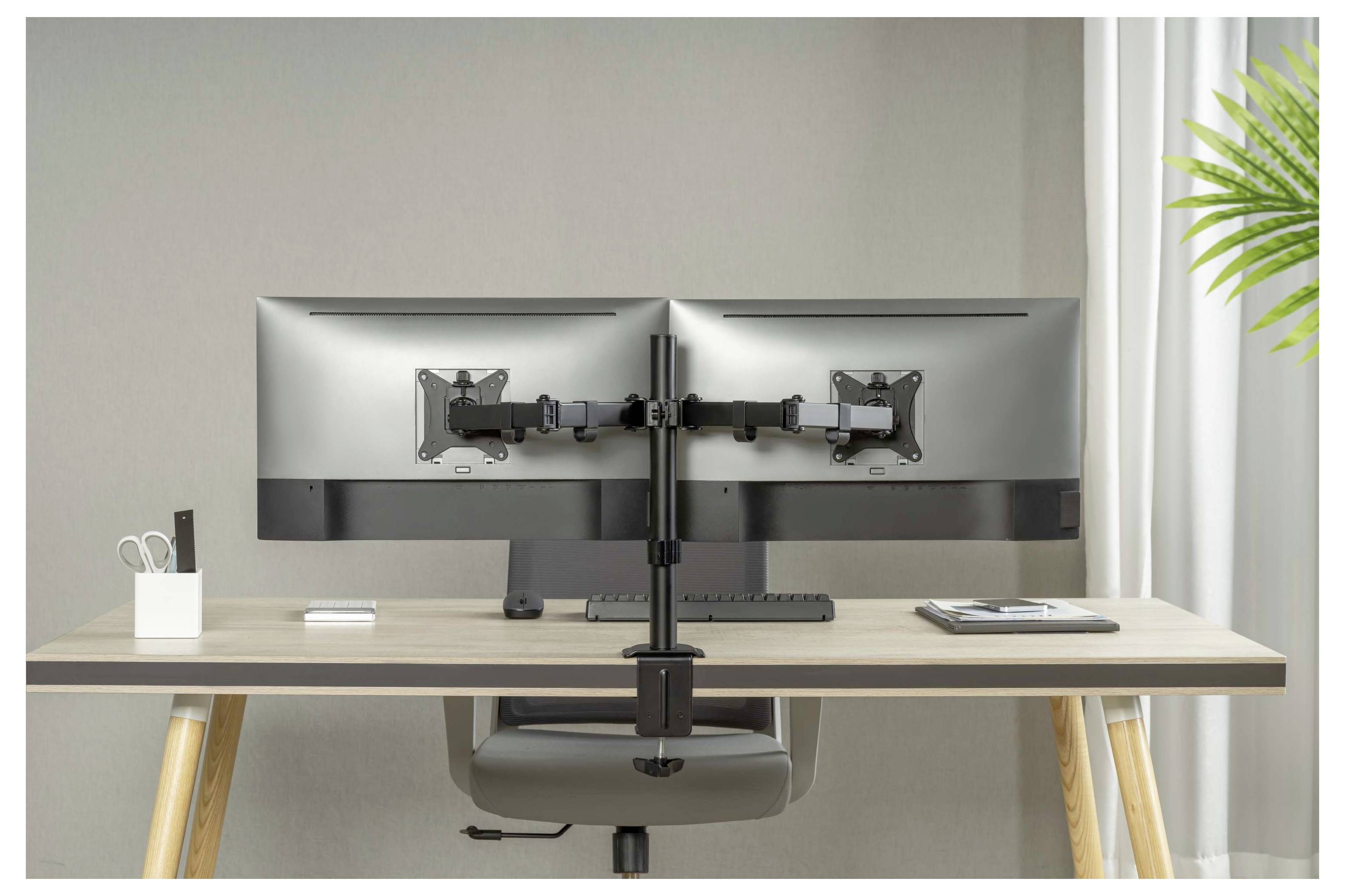 Un espace de travail minimaliste avec une configuration de bureau à double écran comprenant deux moniteurs montés sur un support central, un clavier, une souris, un carnet de notes et de petits accessoires de bureau.