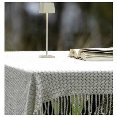 Un livre ouvert posé à côté d'une petite lampe de table se trouve sur une nappe blanche tissée à l'extérieur.