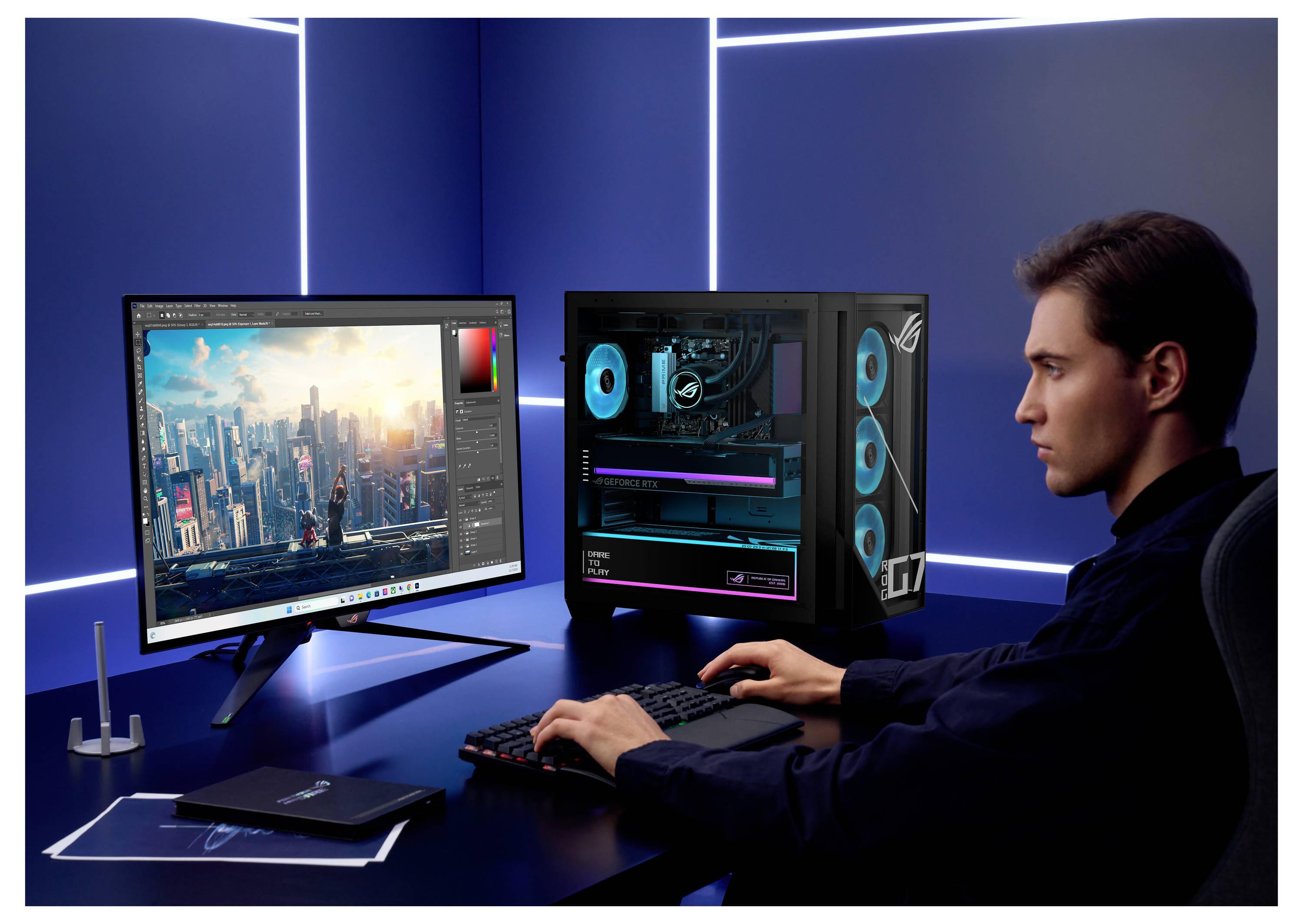 Un homme éditant un paysage urbain futuriste sur un écran d'ordinateur à un bureau avec un ordinateur de jeu et un clavier, dans une pièce éclairée en bleu.