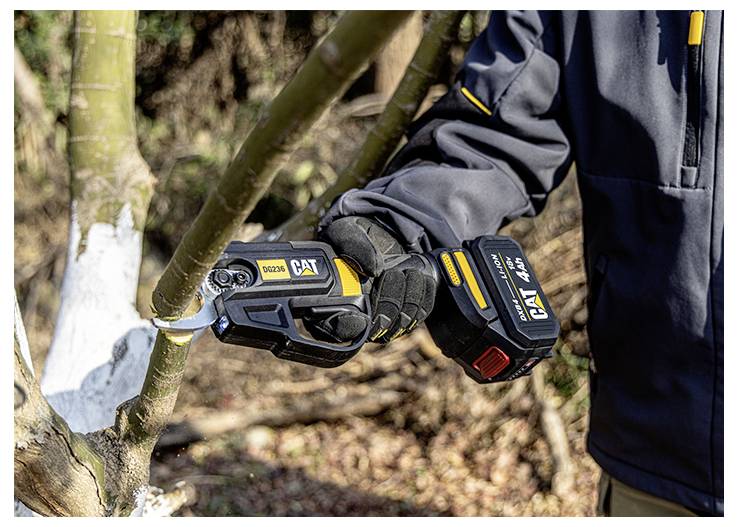 Personne utilisant une scie à élaguer sans fil CAT pour couper une branche d'arbre à l'extérieur, portant des gants et une veste noire.