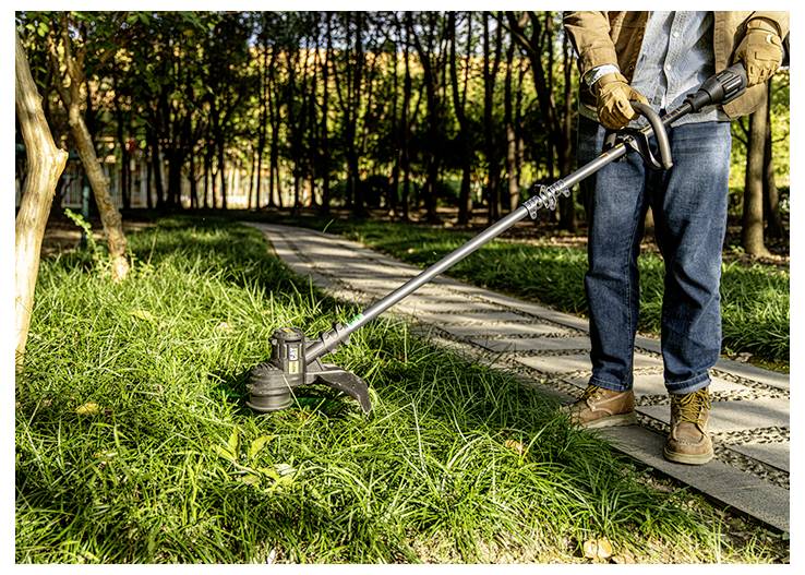 Une personne utilisant un coupe-bordures pour couper l'herbe le long d'un trottoir de parc par une journée ensoleillée.