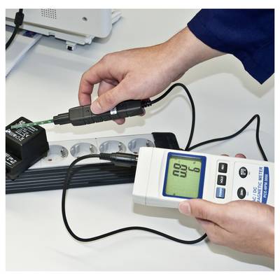 Personne utilisant un multimètre numérique avec une sonde pour mesurer un appareil électrique connecté par des câbles sur un établi.