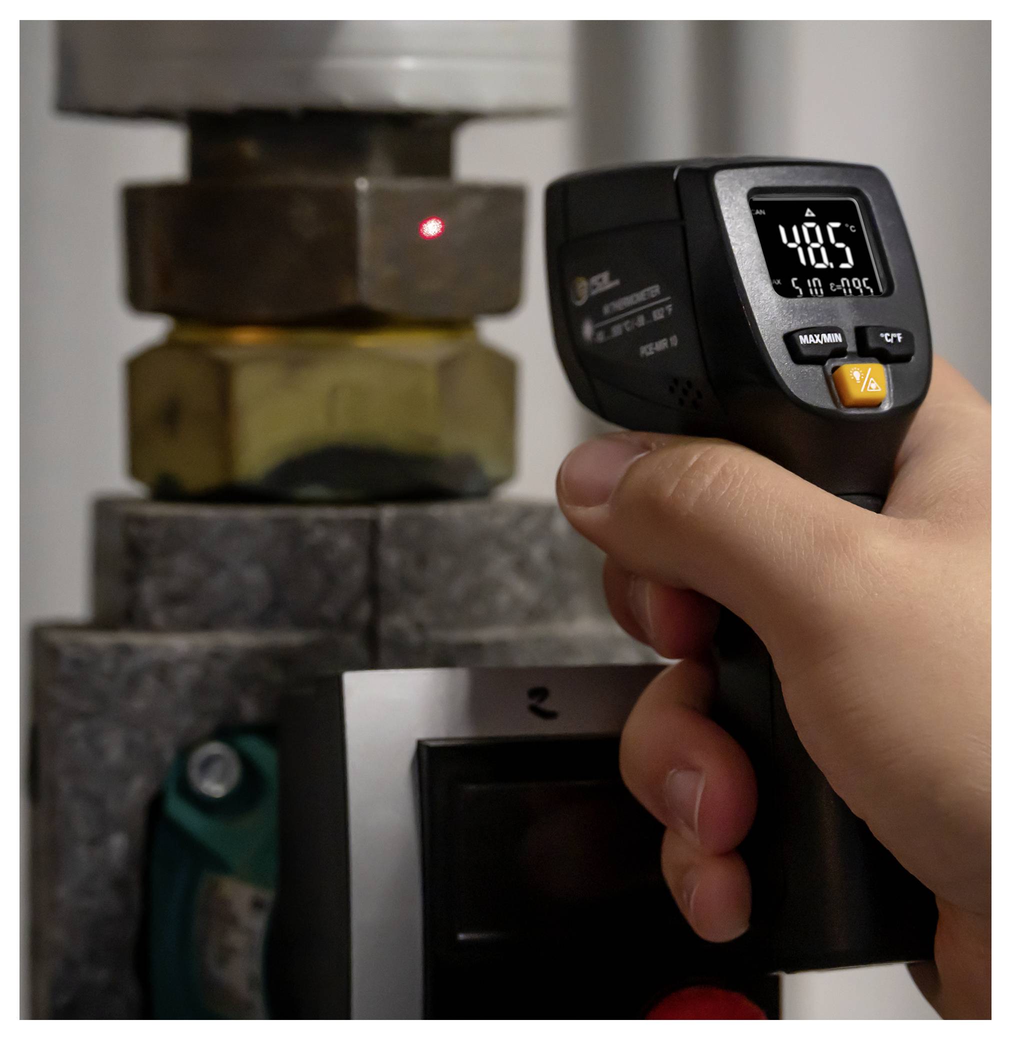 Une main tenant un thermomètre infrarouge pointé vers un robinet en métal chaud, affichant 48,5°C sur l'écran.