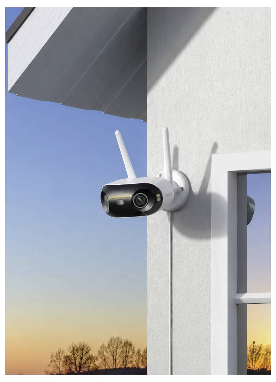 Caméra de sécurité sans fil montée sur l'extérieur d'une maison, orientée vers la cour au coucher du soleil.