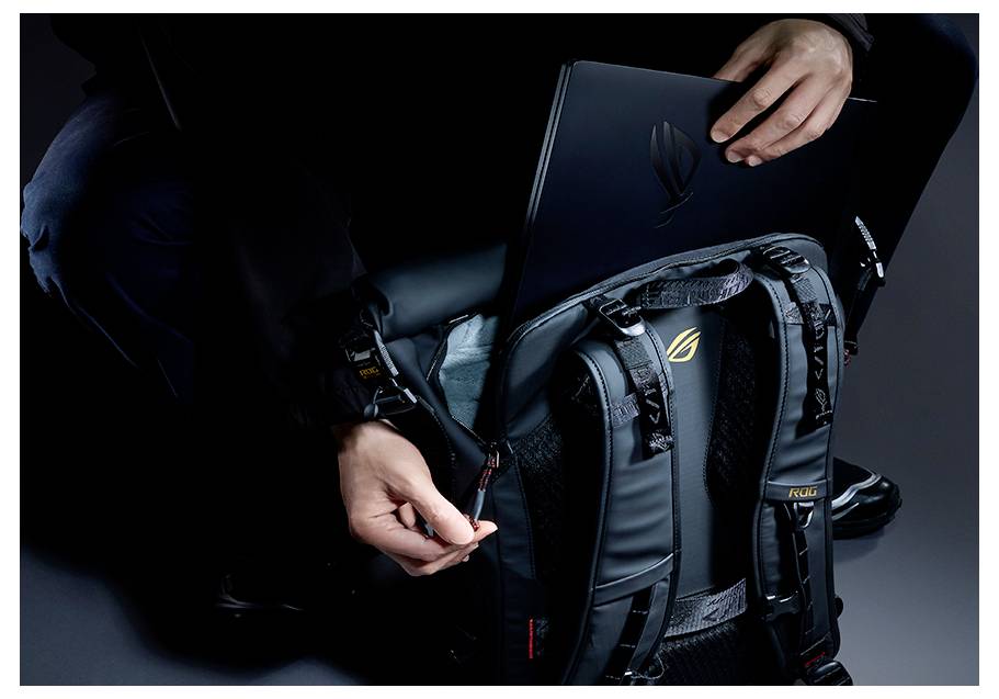 Personne ouvrant un sac à dos ASUS ROG noir et plaçant un ordinateur portable à l'intérieur, montrant les compartiments rembourrés du sac et le logo.