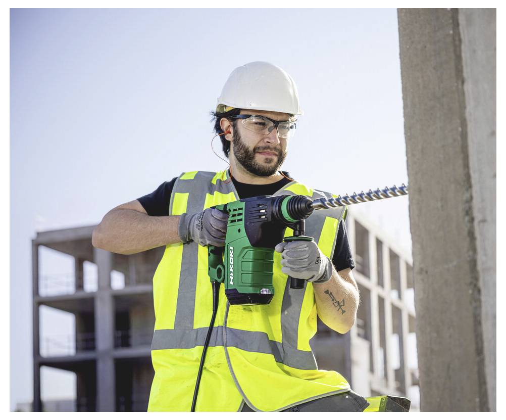 Ouvrier de la construction portant un casque de sécurité et un gilet de haute visibilité utilisant une perceuse électrique sur un chantier de construction.