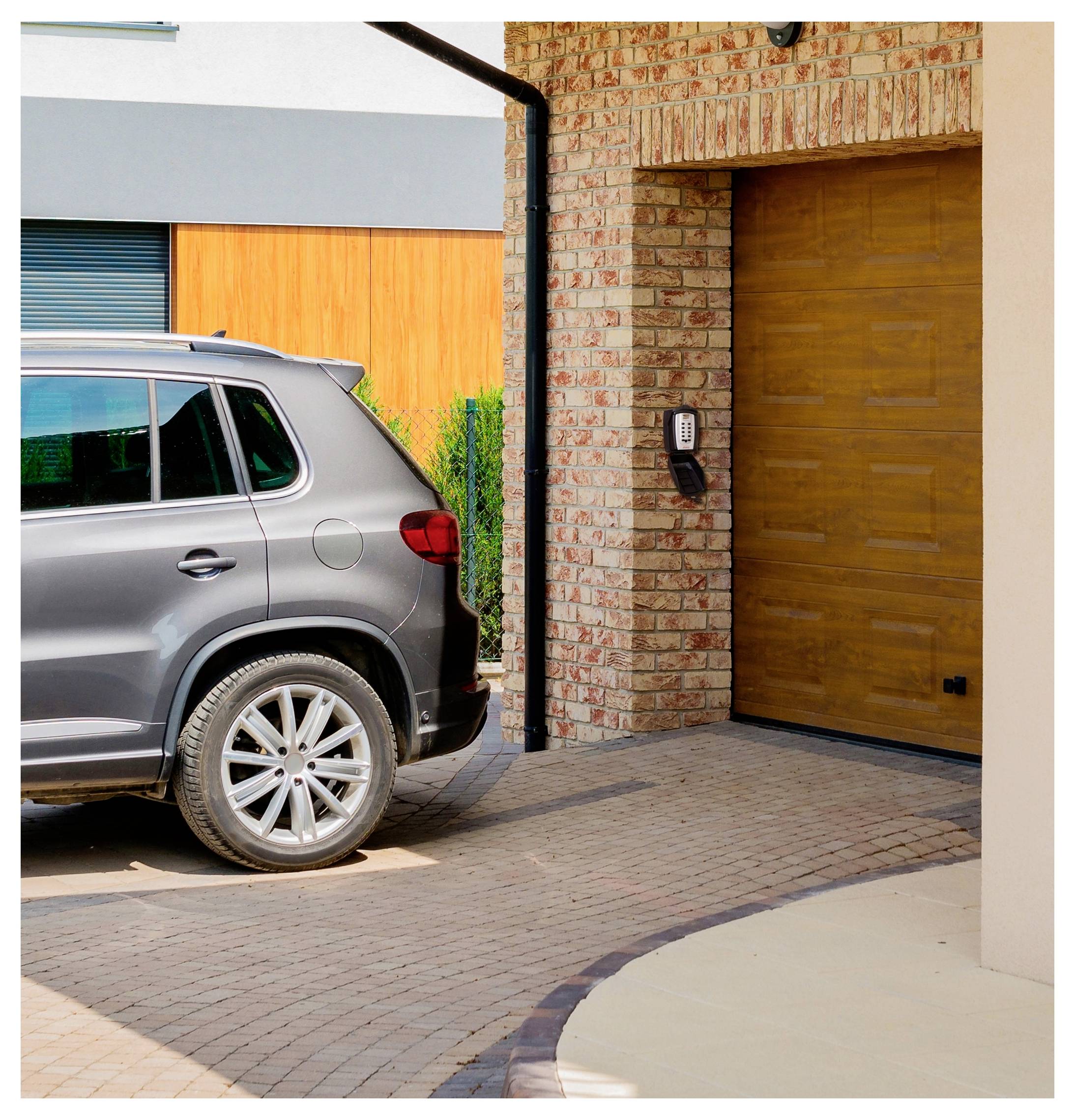 VUS argenté garé à côté d'un garage en brique avec une porte en bois et un clavier numérique sur une allée pavée.