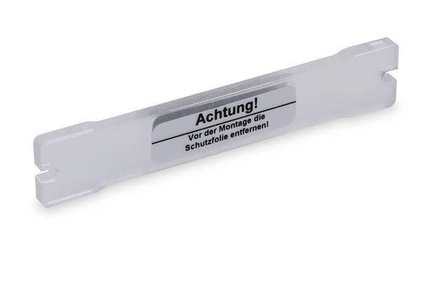 Housse de protection en plastique blanc avec étiquette indiquant « Achtung! Vor der Montage die Schutzfolie entfernen! » sur un fond uni.