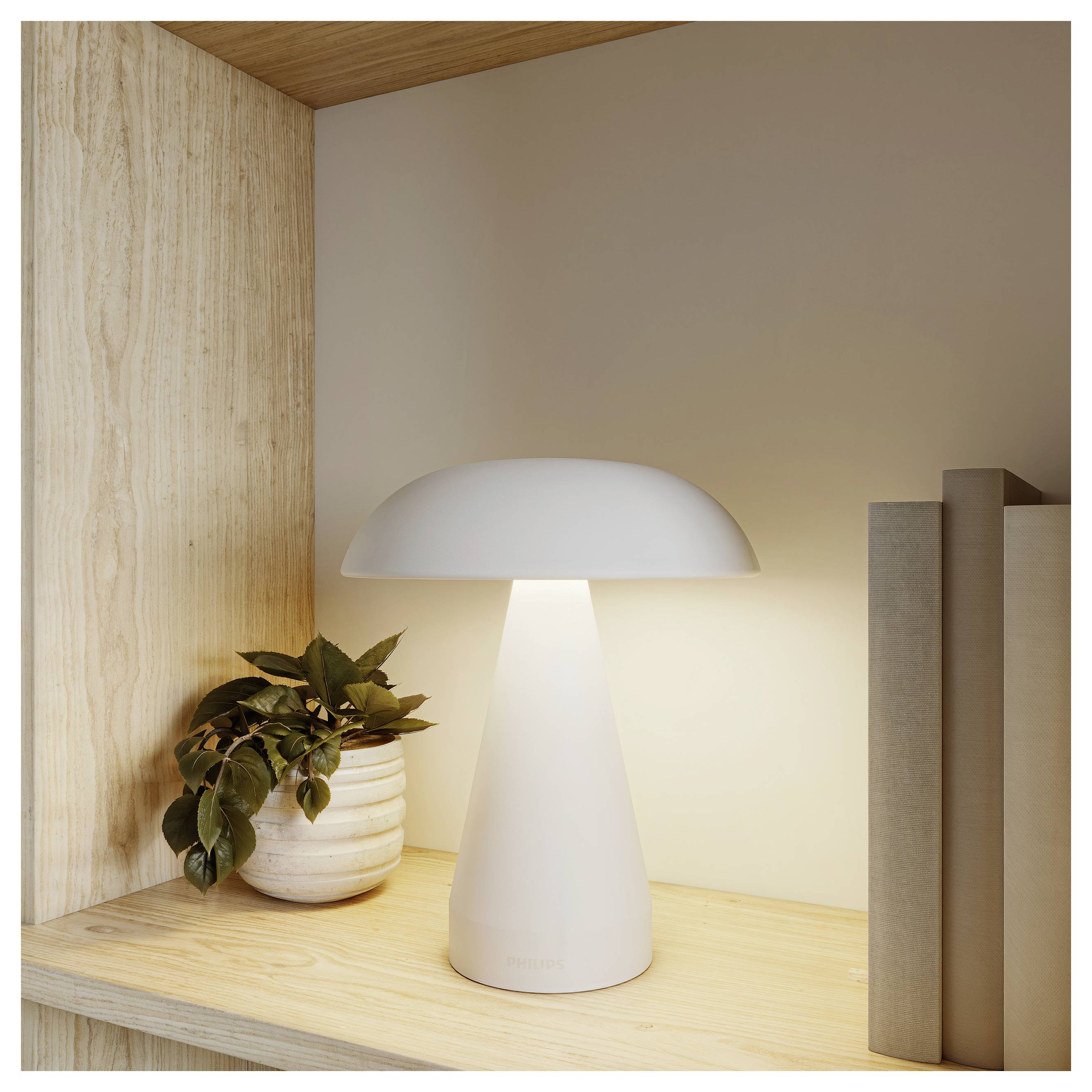 Lampe de table moderne en forme de champignon blanc qui brille sur une étagère en bois à côté d'une plante en pot et de livres dans un coin minimaliste.