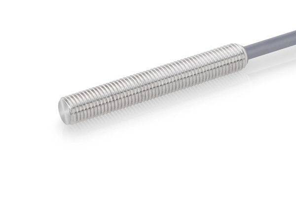 Gros plan d'une sonde métallique cylindrique filetée argentée attachée à un câble sur un fond blanc.