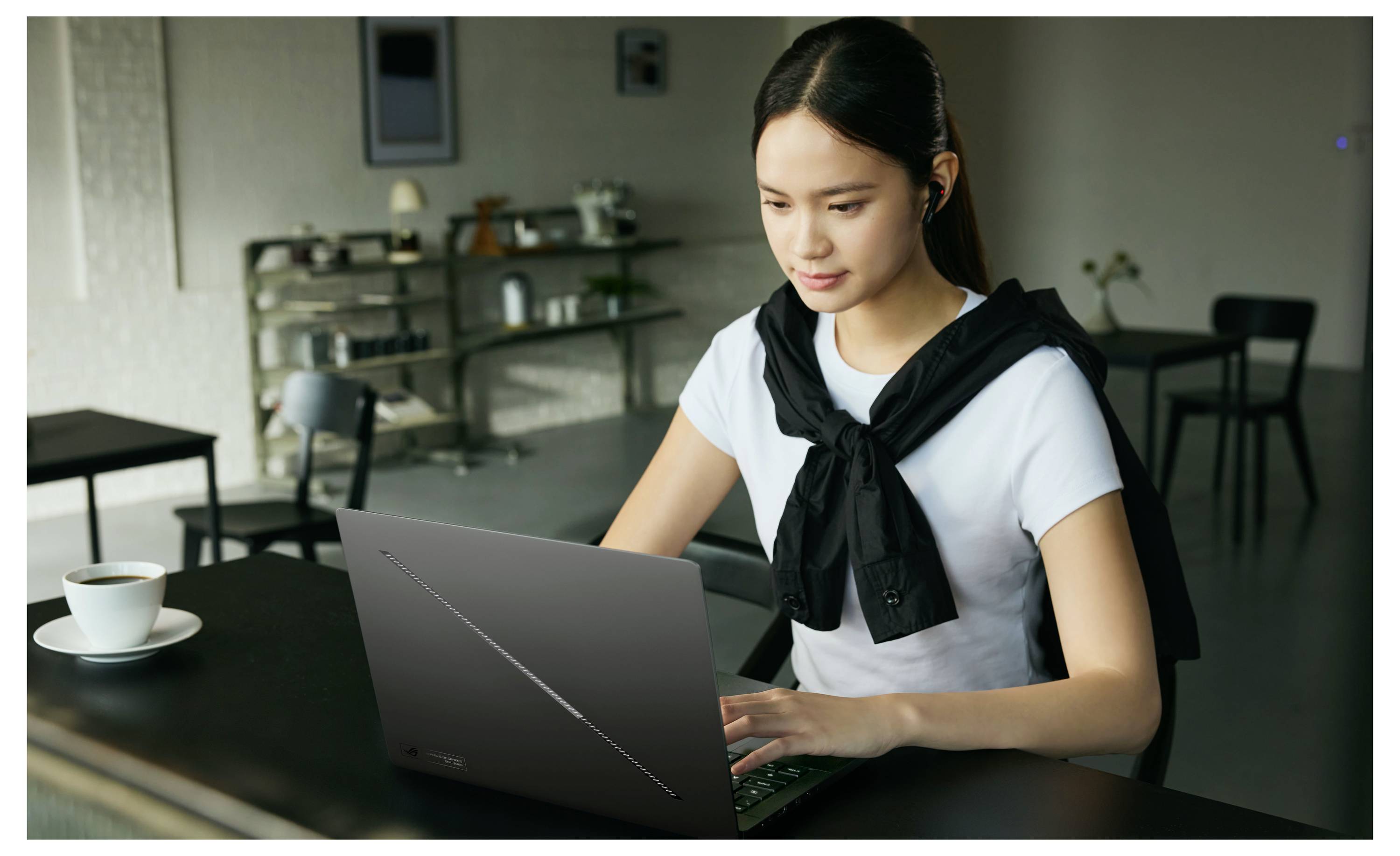 Jeune femme travaillant sur un ordinateur portable à une table de café, avec une tasse de café à côté d'elle.