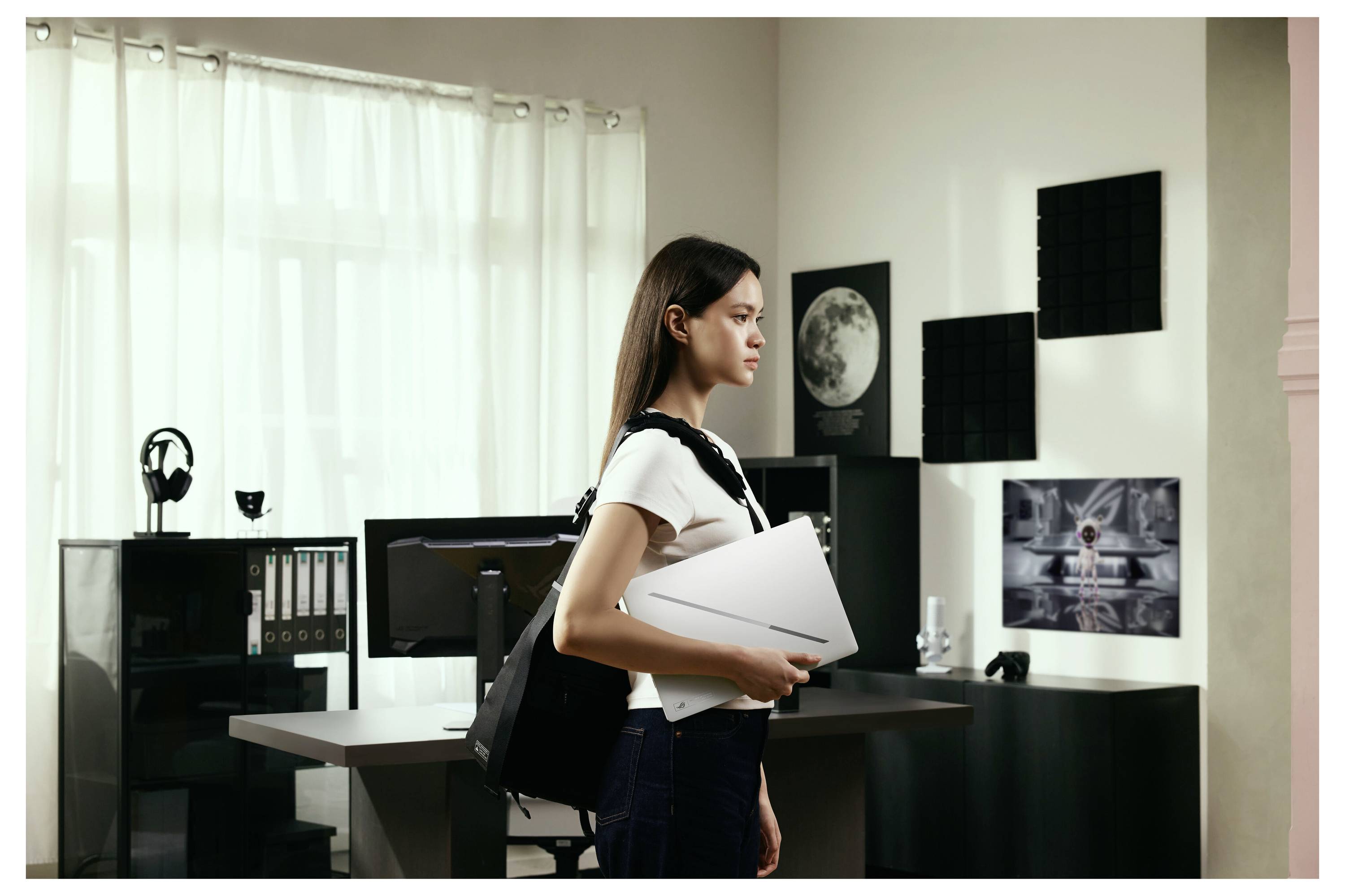 Femme avec sac à dos et dossier debout dans un bureau moderne ou studio avec des bureaux, des moniteurs, des étagères et des œuvres d'art murales