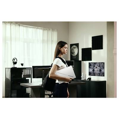 Femme avec sac à dos et dossier debout dans un bureau moderne ou studio avec des bureaux, des moniteurs, des étagères et des œuvres d'art murales