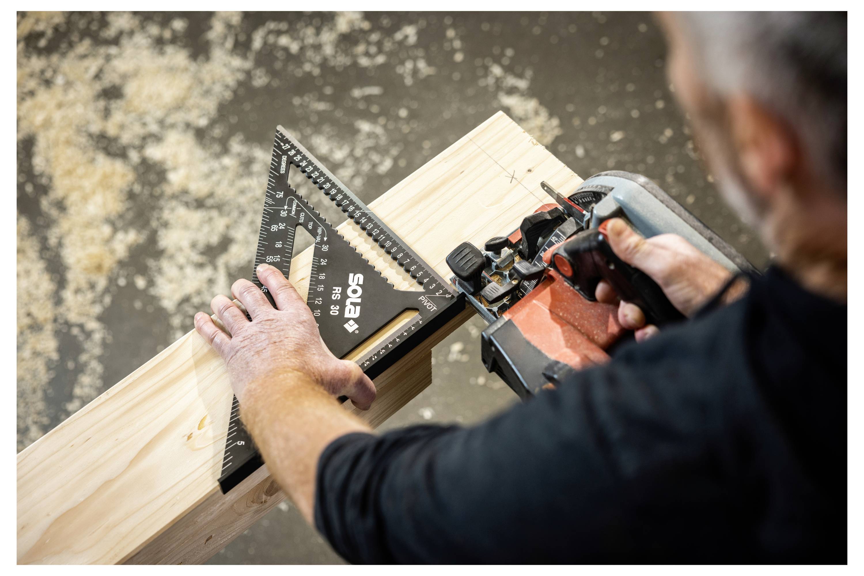 Personne utilisant une scie électrique et une équerre pour couper avec précision une poutre en bois sur un établi.