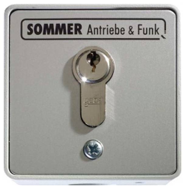 Panneau de commutateur à clé en métal étiqueté « SOMMER Antriebe & Funk » avec une clé insérée au centre et une vis en dessous.