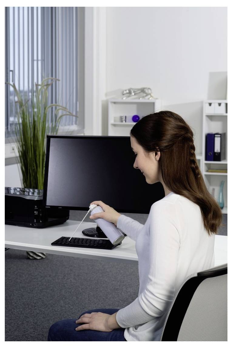 Une femme dans un bureau nettoie un clavier d'ordinateur avec un chiffon à côté d'un moniteur et d'un bureau.