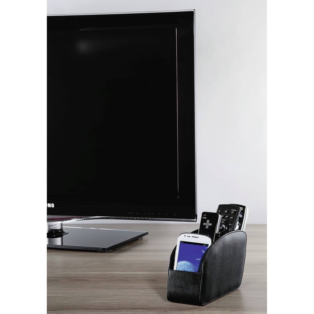 Bureau avec un grand moniteur et un organiseur noir contenant un smartphone et des télécommandes sur une surface en bois.