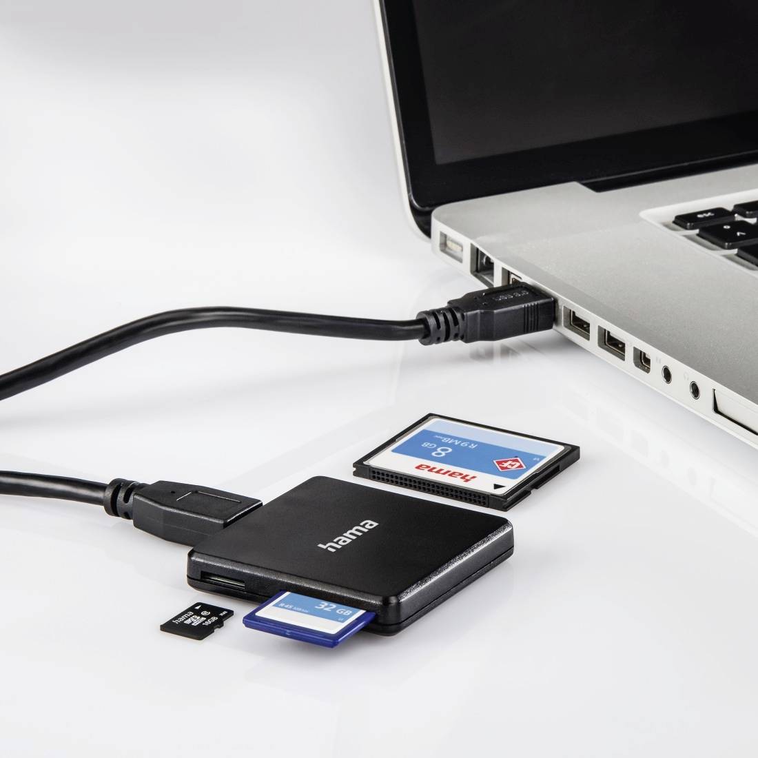 Ordinateur portable connecté par câble à un lecteur de cartes Hama avec des cartes mémoire SD et microSD insérées sur une surface blanche.