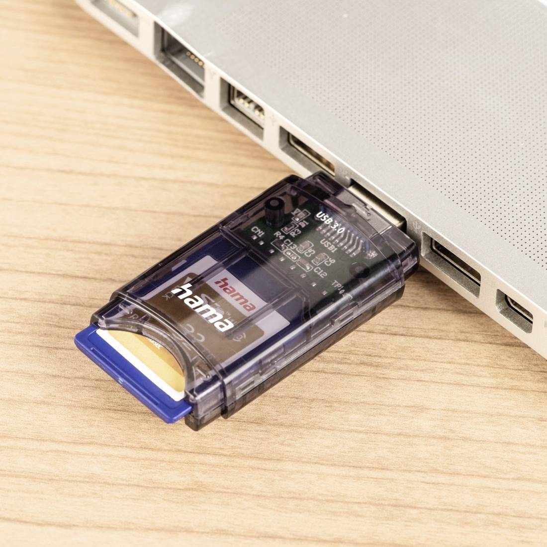Lecteur de cartes USB branché sur le port d'un ordinateur portable sur un bureau en bois, avec une carte SD insérée.