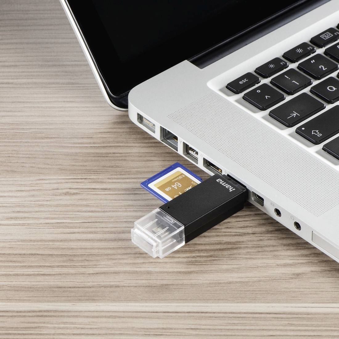 Clé USB et carte SD insérées dans les ports latéraux d'un ordinateur portable sur un bureau en bois.