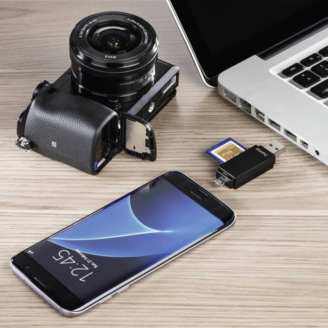 Un appareil photo avec objectif, des cartes mémoire, une clé USB, un smartphone et un ordinateur portable disposés sur un bureau pour transférer ou stocker des photos et des fichiers.