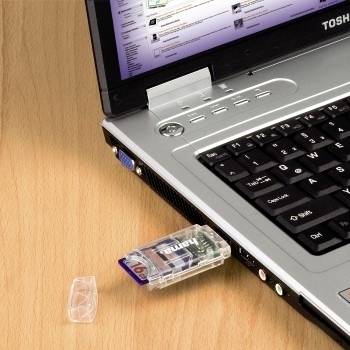 Un ordinateur portable Toshiba sur un bureau en bois avec une clé USB branchée sur le côté et son capuchon gisant à proximité.