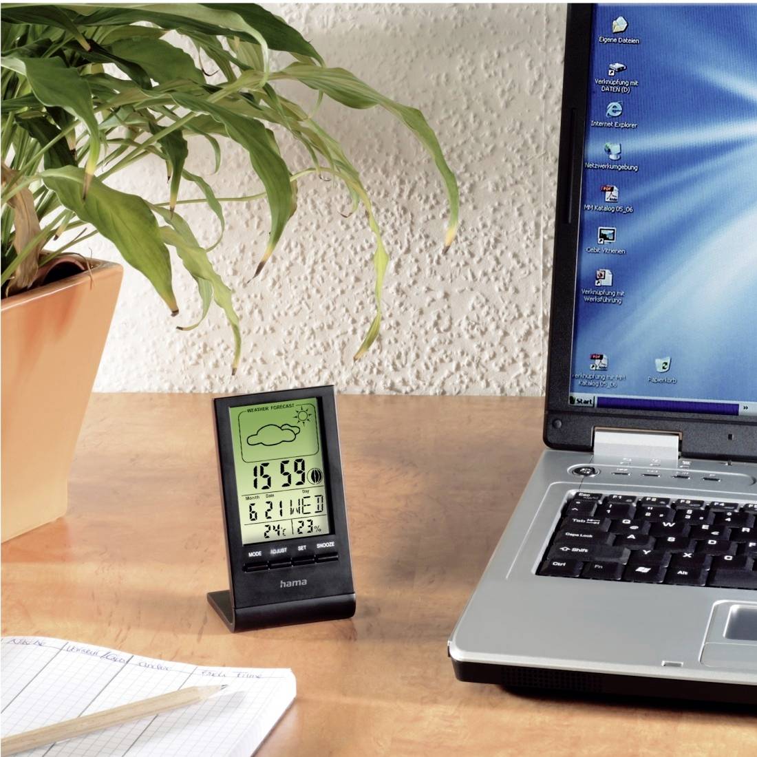 Scène de bureau avec un ordinateur portable, une horloge numérique affichant 15:59, une plante en pot et un bloc-notes sur un bureau en bois.
