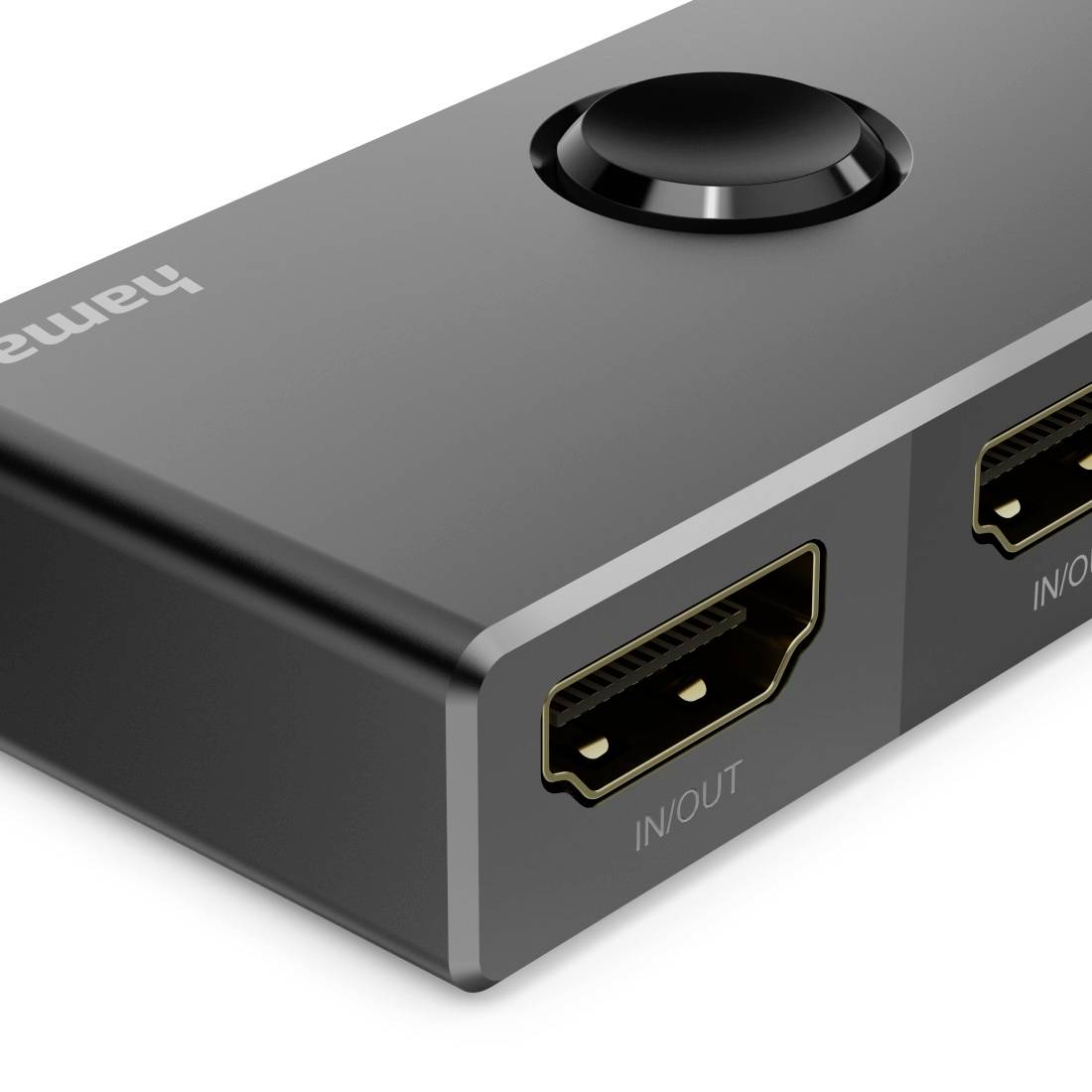 Gros plan d'un boîtier commutateur HDMI noir avec un bouton rond sur le dessus et deux ports HDMI étiquetés « IN/OUT ».