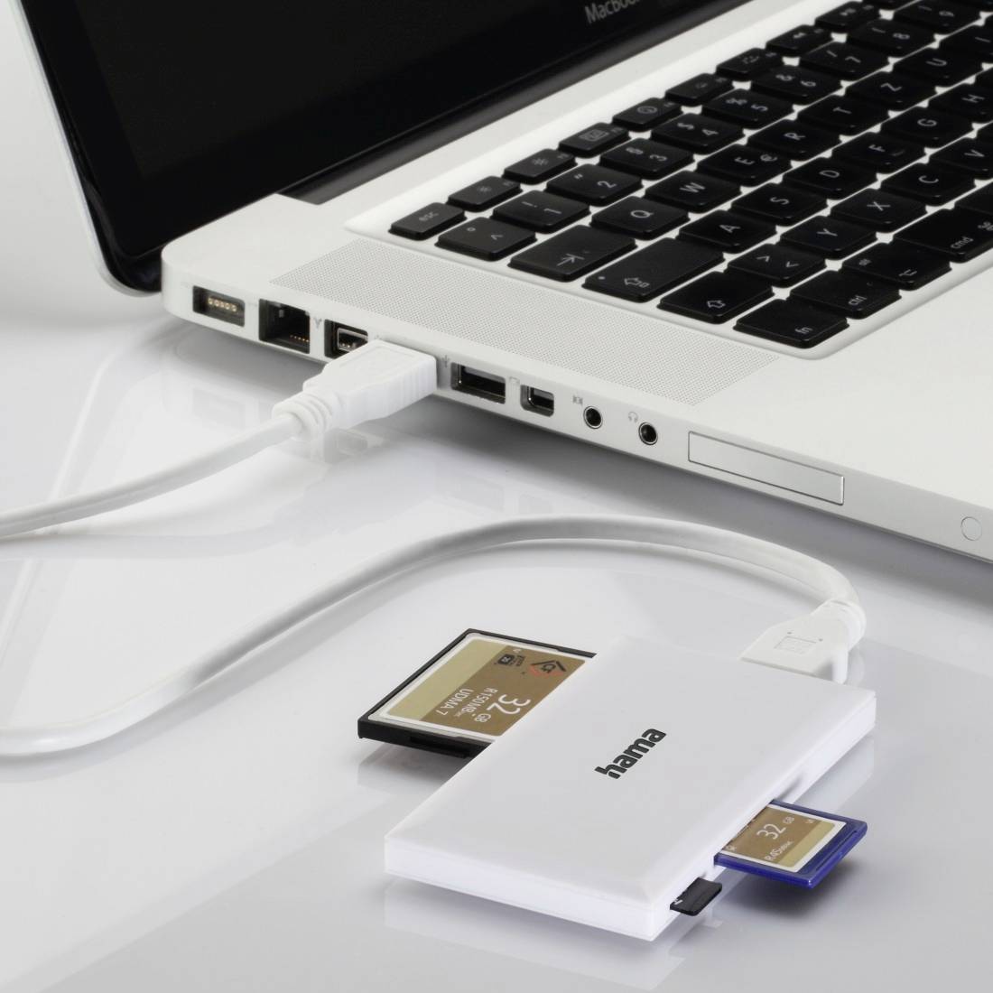 Ordinateur portable avec un lecteur de cartes USB connecté, affichant des cartes mémoire SD insérées sur une surface blanche.