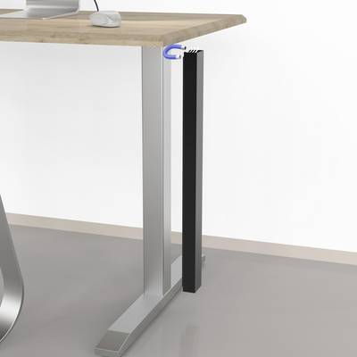 Dessous du bureau avec un bac de gestion des câbles noir vertical attaché au bord, à côté d'un pied de table en métal argenté sur un poste de travail en bois clair.