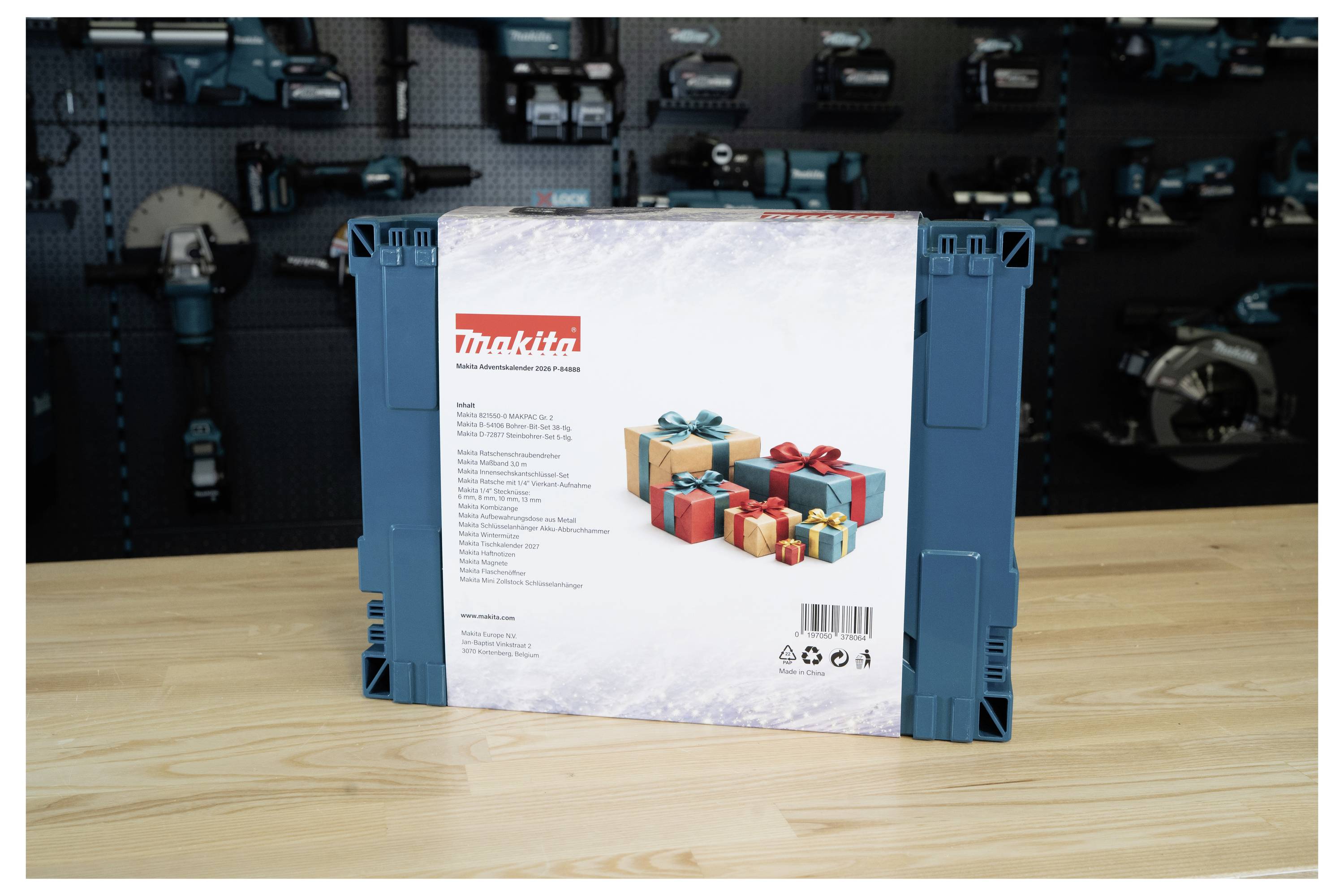 Un ensemble d'outils de marque Makita en boîte ou un étui, présenté verticalement sur une table en bois devant un mur flou d'outils électriques.