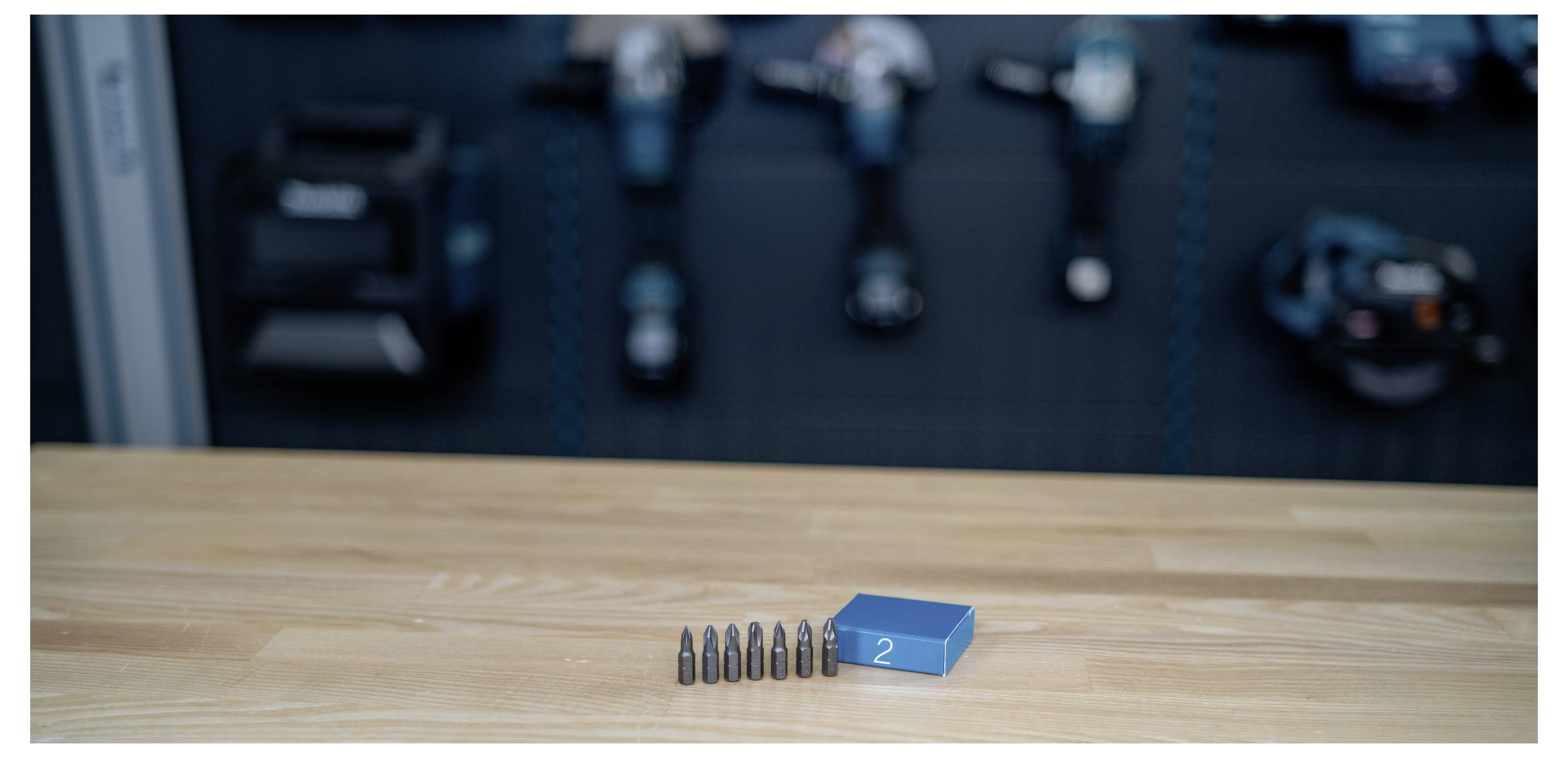 Une rangée de six balles et une boîte bleue étiquetée « 2 » sur une table en bois, avec des composants de pistolet flous en arrière-plan.