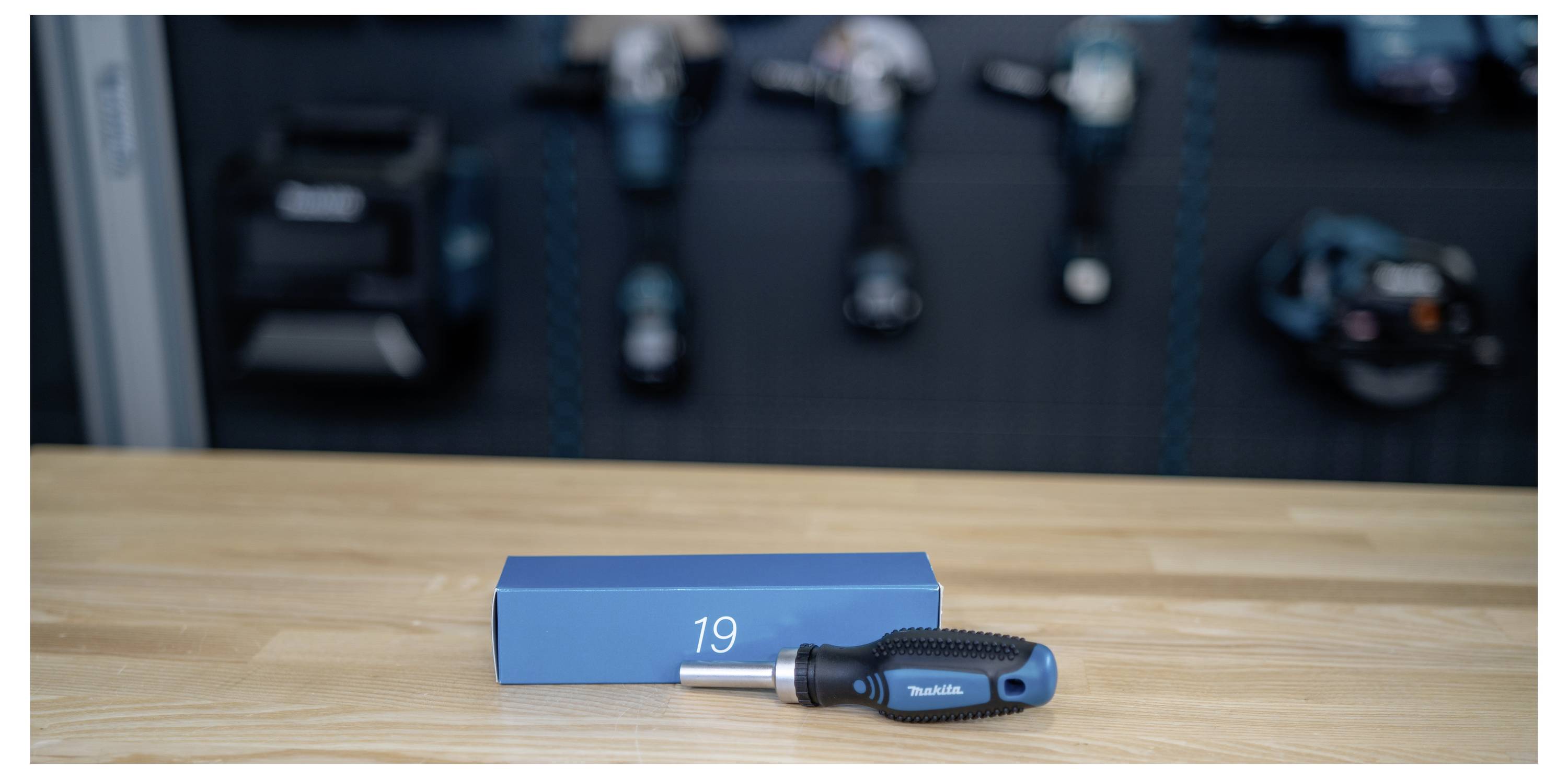 Boîte bleue étiquetée « 19 » et un tournevis sur un établi en bois, avec des outils flous en arrière-plan.