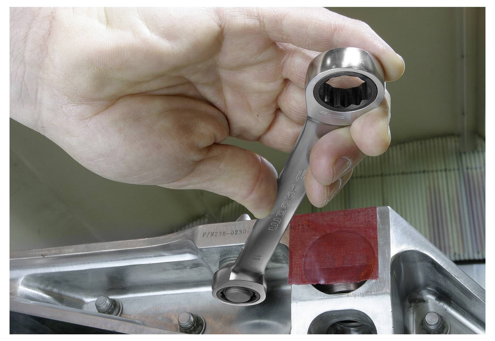 Une main utilisant une clé à cliquet sur un boulon dans un assemblage de machine en métal, avec une zone marquée en rouge indiquant le fixateur en cours d'ajustement.