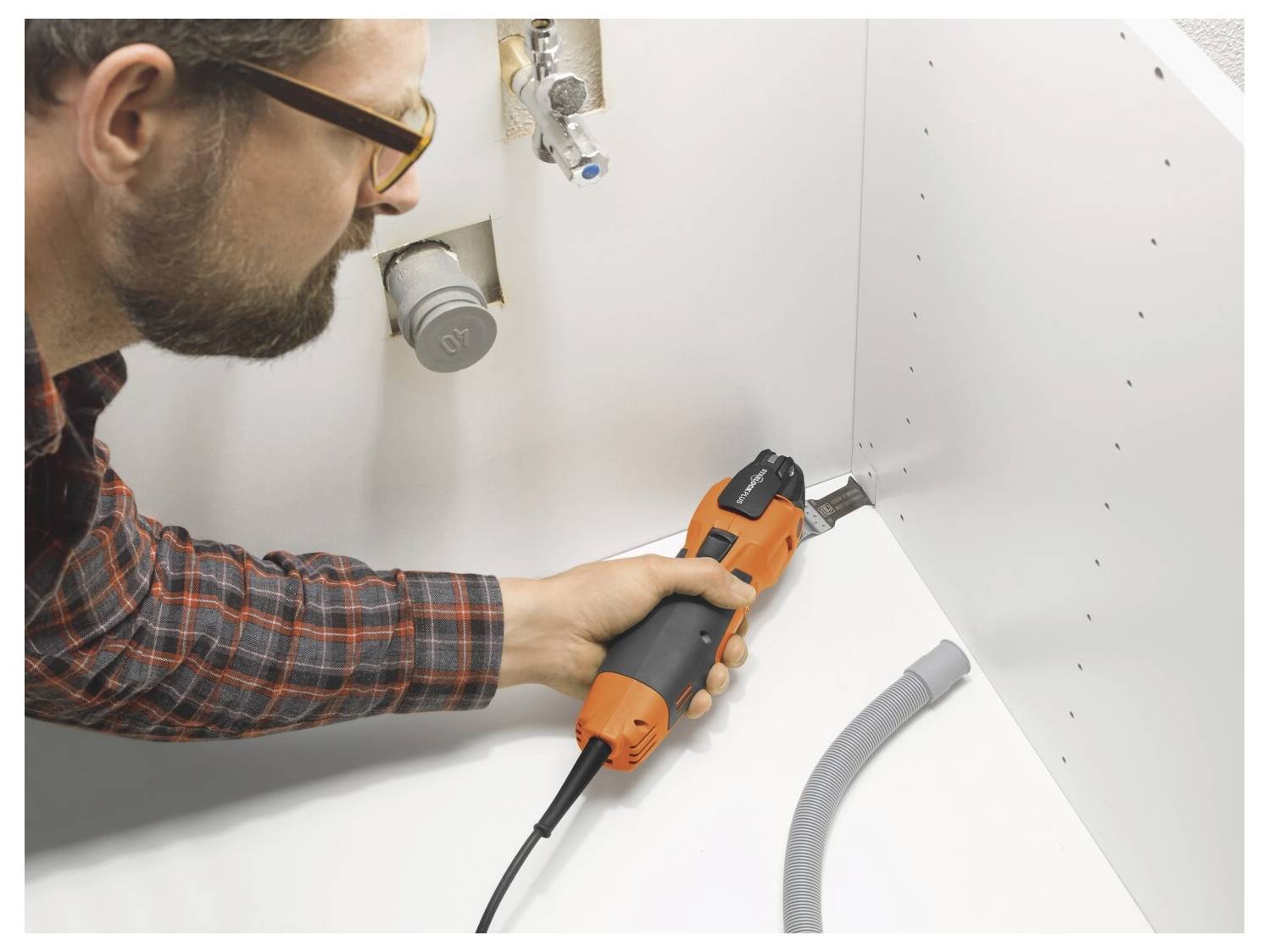 Un homme utilise une perceuse orange pour installer une vis dans un placard blanc ou un panneau mural pendant l'assemblage à domicile.