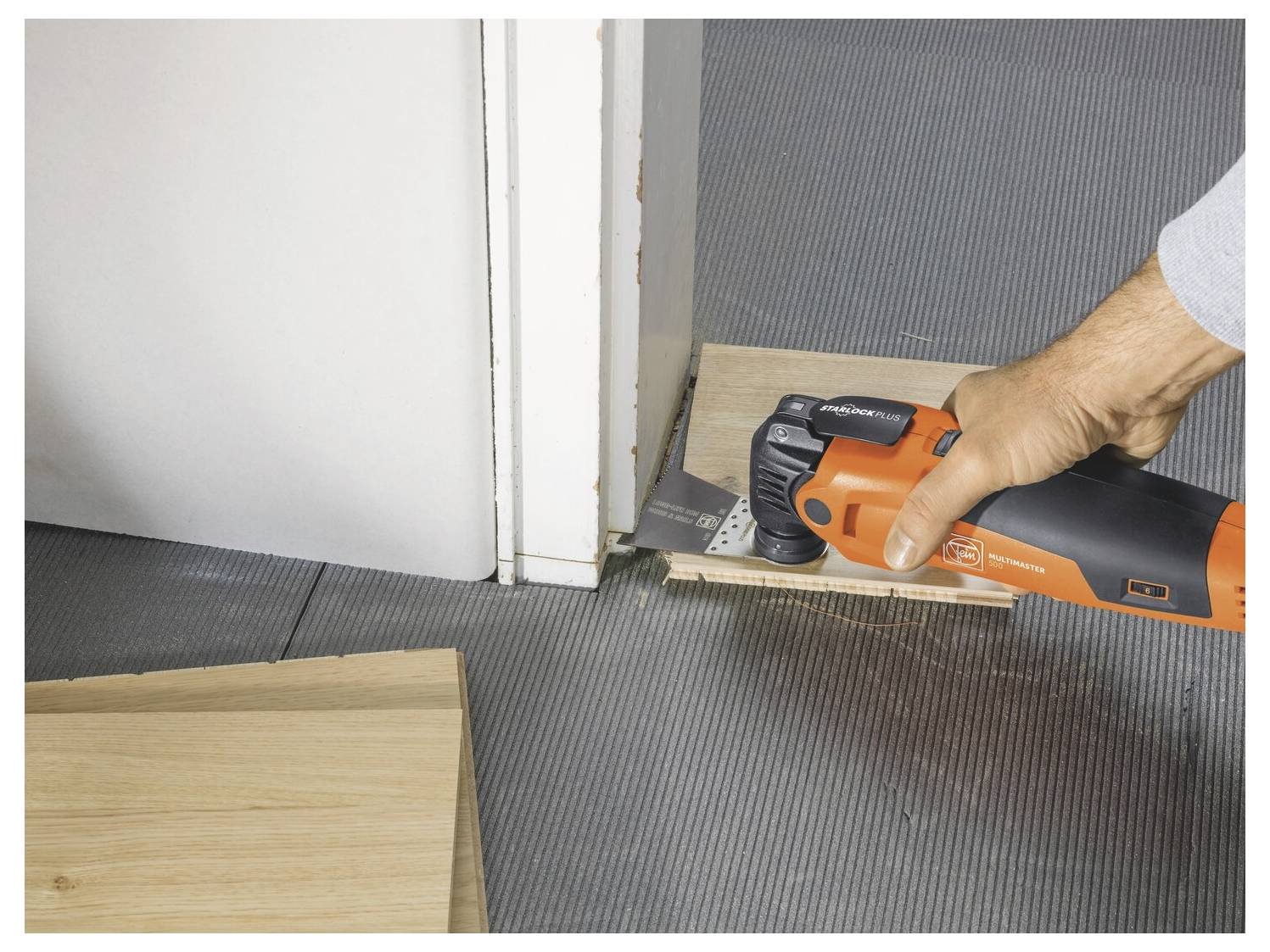 Une main utilisant un outil électrique pour couper ou tailler une planche de plancher à l'entrée d'une porte lors de l'installation du revêtement de sol.
