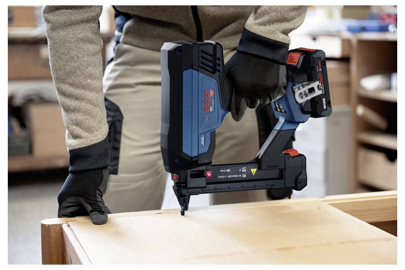 Personne utilisant un pistolet à clous sans fil pour fixer une planche en bois lors de travaux de menuiserie.