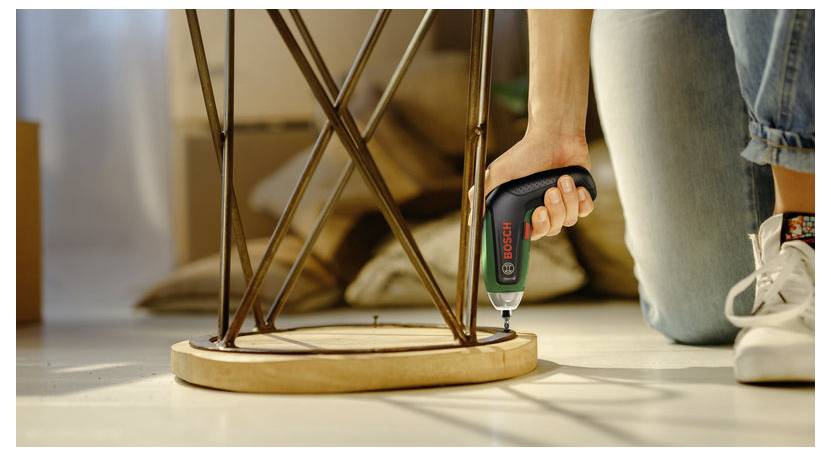 Une personne utilise un tournevis sans fil Bosch pour fixer la base d'une petite table ou d'un tabouret lors du montage de meubles.