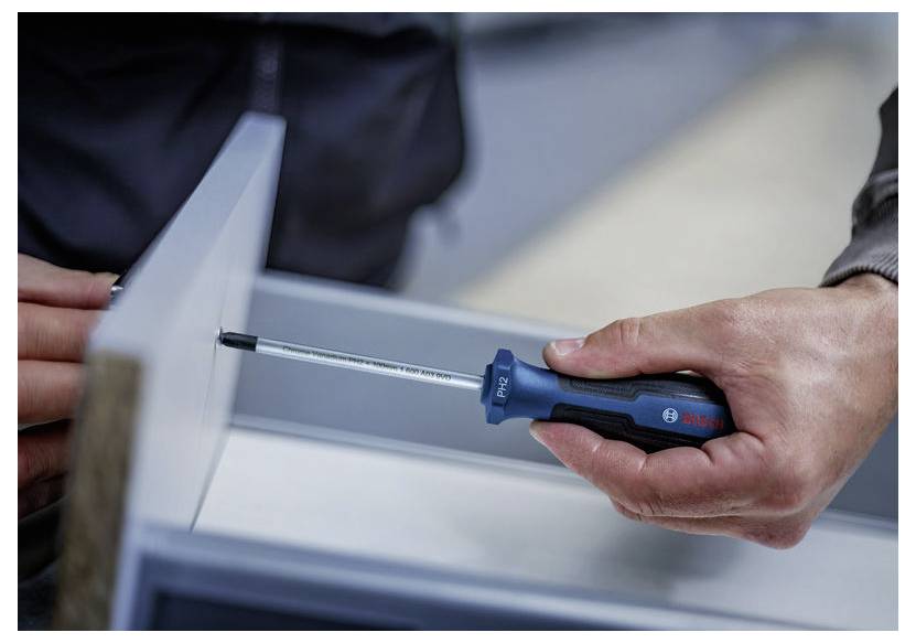 Gros plan des mains utilisant un tournevis Bosch pour serrer une vis sur un panneau métallique ou un cadre d'appareil.