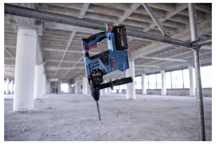 Perceuse-burin rotatif sans fil bleue suspendue à une poutre de plafond dans l'intérieur d'un bâtiment en béton brut non fini.