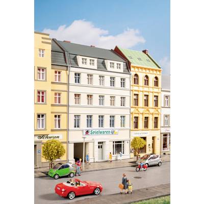 Scène de rue avec des immeubles mitoyens colorés de style européen abritant des commerces, des piétons sur le trottoir, et plusieurs voitures, y compris une décapotable rouge et une petite voiture verte compacte.